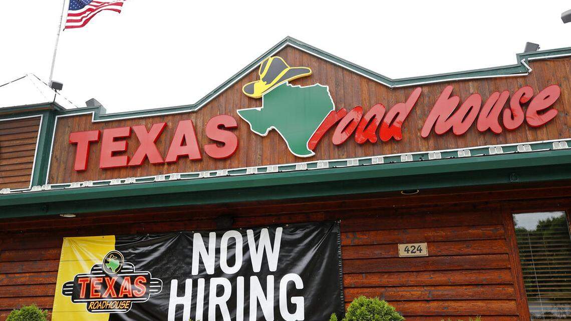 A “Now Hiring” sign Is displayed outside a Texas Roadhouse restaurant, Friday, June 5, 2020, in Methuen, Mass. The family of Texas Roadhouse CEO Kent Taylor said in a statement he died by suicide while experiencing lingering symptoms from COVID-19, including tinnitus.