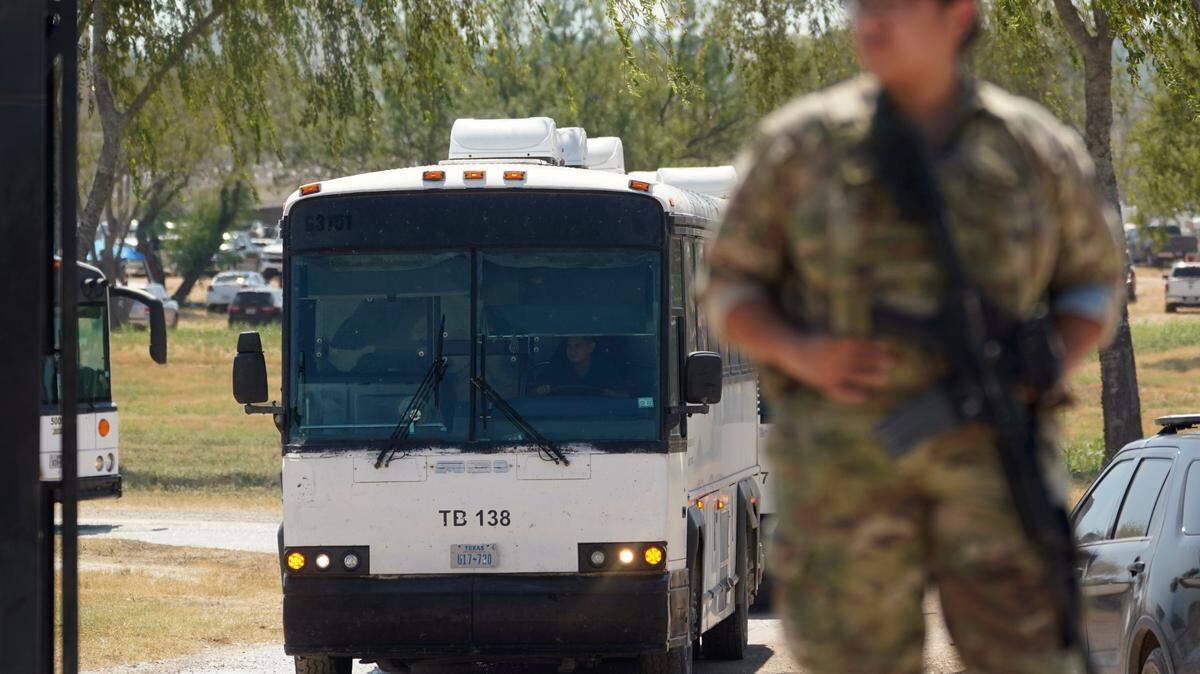 A National Guardsman stands at a gate along a border fence as a bus used to transport migrants, mostly from Haiti, departs from a makeshift camp that has developed at the International Bridge on Sept. 20, 2021, in Del Rio, Texas.
