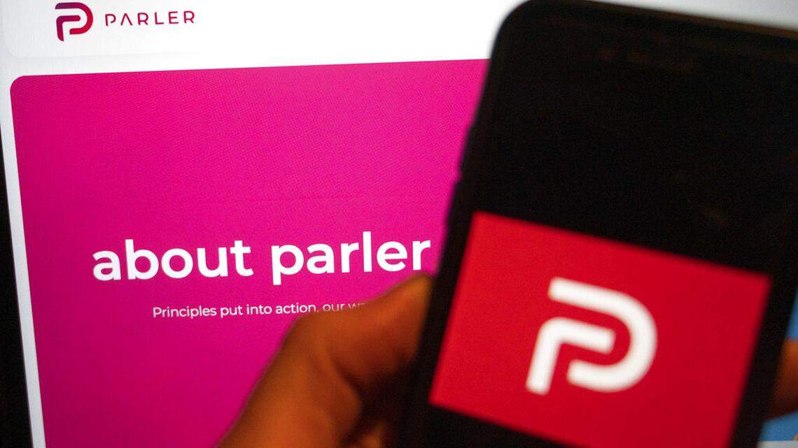 The logo of the social media platform Parler is displayed in Berlin, Jan. 10, 2021. In the background on a screen is the platform’s website. The conservative-friendly social network Parler was booted off the internet Monday, Jan. 11, over ties to last week’s siege on the U.S. Capitol, but not before hackers made off with an archive of its posts, including any that might have helped organize or document the riot. (Christophe Gateau/dpa via AP)