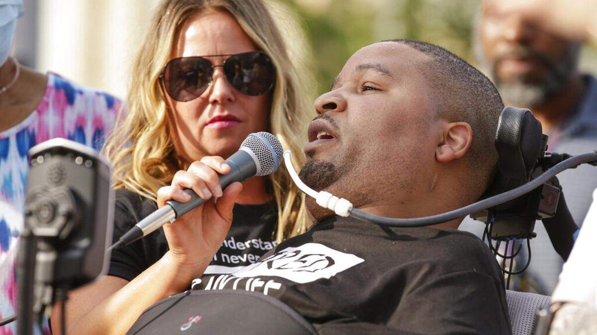 In this June 6, 2020, photo, Jerime Mitchell speaks to the crowd as his wife Bracken holds the microphone during a protest against police brutality at Greene Square in Cedar Rapids, Iowa. An insurance company for the City of Cedar Rapids will pay $8 million to Mitchell, who was paralyzed after police officer Lucas Jones shot him during a 2016 traffic stop.