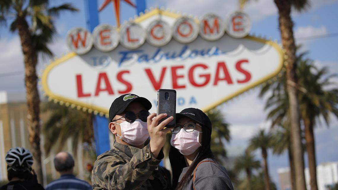 A couple wearing face masks take a selfie at the “Welcome to Fabulous Las Vegas Nevada” sign amid a shutdown of casinos along the Las Vegas Strip due to coronavirus Saturday, March 21, 2020, in Las Vegas. (AP Photo/John Locher)