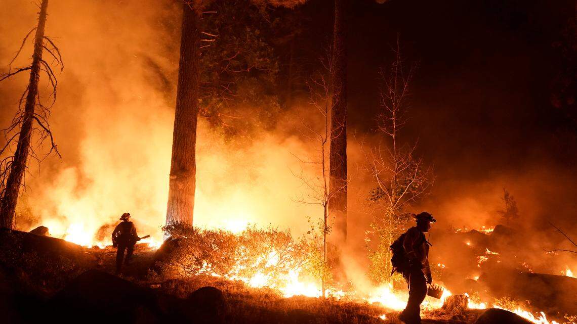 Two firefighters monitor the Caldor Fire burning near homes in South Lake Tahoe, Calif., Monday, Aug. 30, 2021. As the winds returned this week, the Caldor Fire roared over the Sierra crest and bore down on the southern end of Lake Tahoe. (AP Photo/Jae C. Hong)