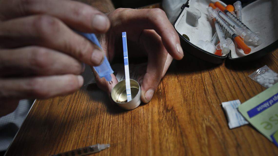An addict prepares heroin, placing a Fentanyl test strip into the mixing container to check for contamination.
