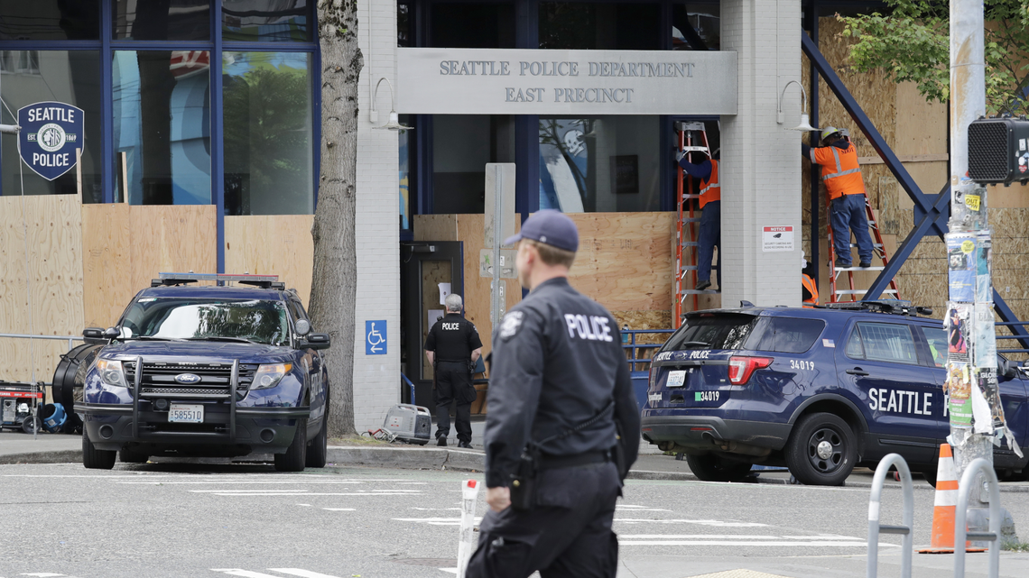 Workers put up plywood over the windows of a Seattle police precinct Monday, June 8, 2020, in Seattle, where protests continued the night before over the death of George Floyd. Now, five months after Floyd’s death, protests are still ongoing in Seattle.