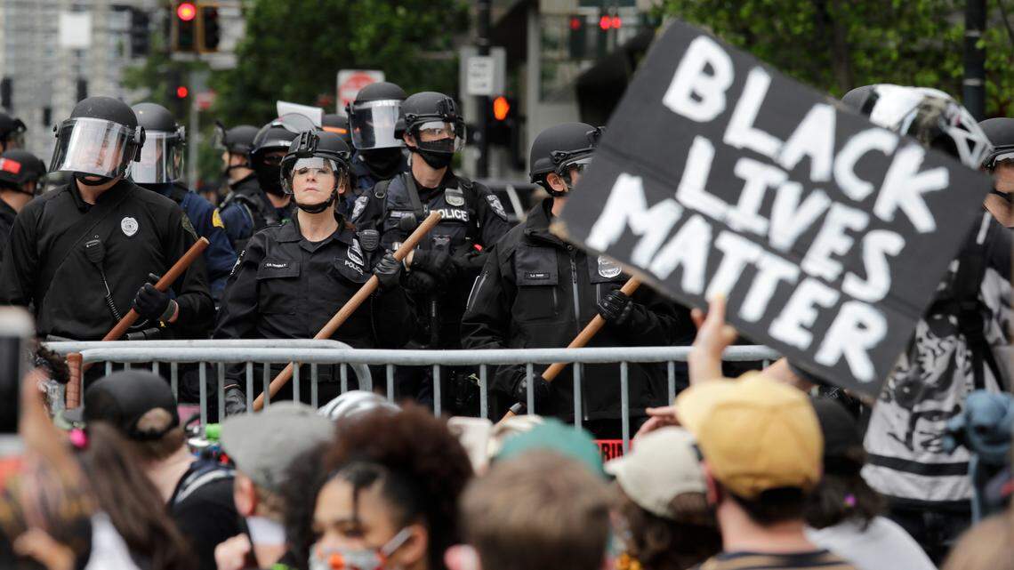 In this June 3, 2020, file photo, police officers behind a barricade look on as protesters fill the street in front of Seattle City Hall in Seattle. A Seattle man filed a federal civil rights lawsuit accusing police of using excessive force against him and his son during a 2020 Black Lives Matter protest.