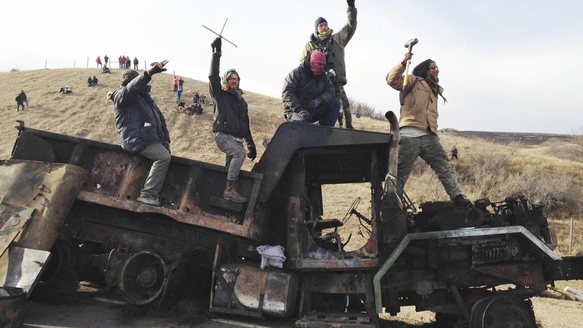 Protesters against the Dakota Access oil pipeline stand on a burned-out truck near Cannon Ball, N.D., Monday, Nov. 21, 2016, that they removed from a long-closed bridge on Sunday on a state highway near their camp in southern North Dakota. Opponents skirmished with law officers late Sunday and early Monday.