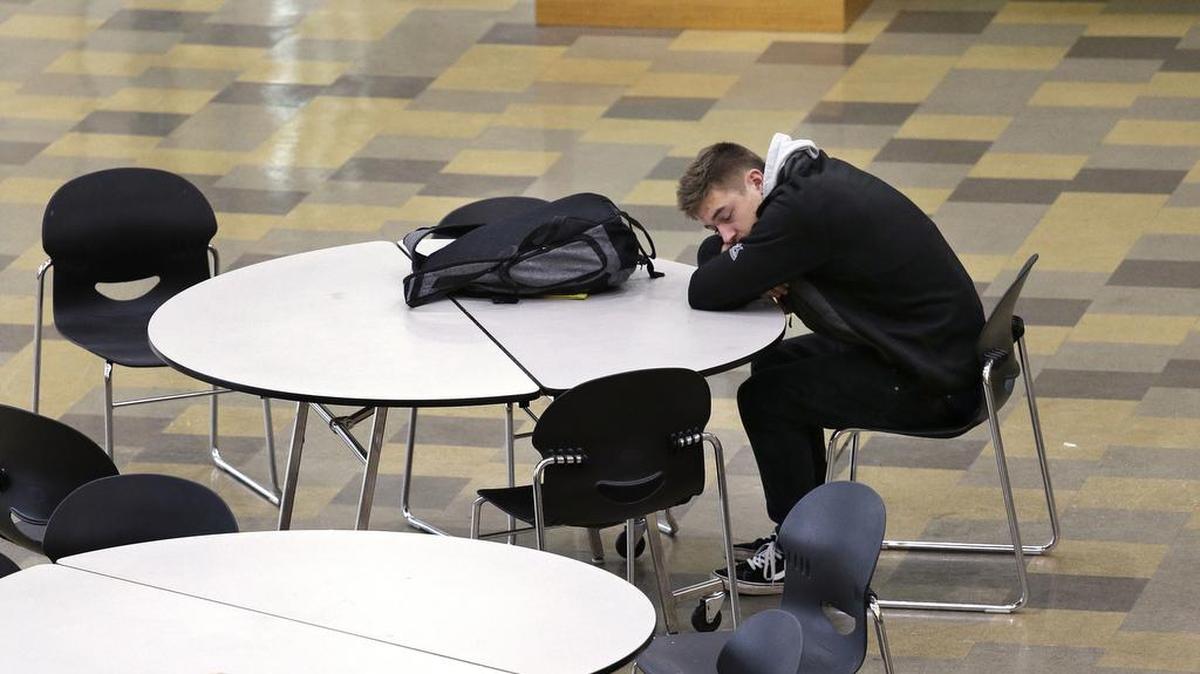 In this photo taken Nov. 23, 2015, a student leans on a table in the cafeteria during first period at Roosevelt High School in Seattle. More school districts around the U.S. are heeding the advice of scientists who have long said that expecting teens to show up to class before 8 a.m. isn’t good for their health or their report cards.