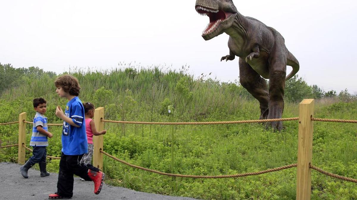 FILE - In this Friday, May 25, 2012 file photo, children stand near a life-size Tyrannosaurus Rex dinosaur model as it moves and growls in an interactive display at Field Station Dinosaurs in Secaucus, N.J.