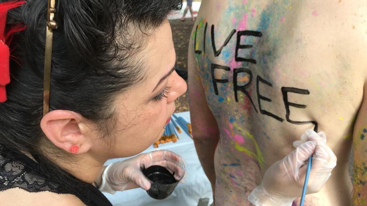 Artist Nicole Tossas paints a slogan on the back of a bicyclist before the annual Philly Naked Bike Ride in Philadelphia on Saturday Sept. 10, 2016. Thousands of bicyclists dared to be bare for the city's annual nude ride promoting positive body image, cycling advocacy and fuel conservation.