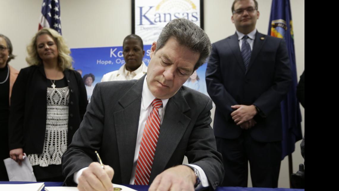 
Gov. Sam Brownback signs a welfare reform bill into law in Topeka, Kan., Thursday, April 16, 2015. The law tells recipients that they can’t use cash assistance from the state to attend concerts, get tattoos or buy lingerie. Although more than 20 states have similar bills, Kansas appears to have the most extensive list of restricted items. 
