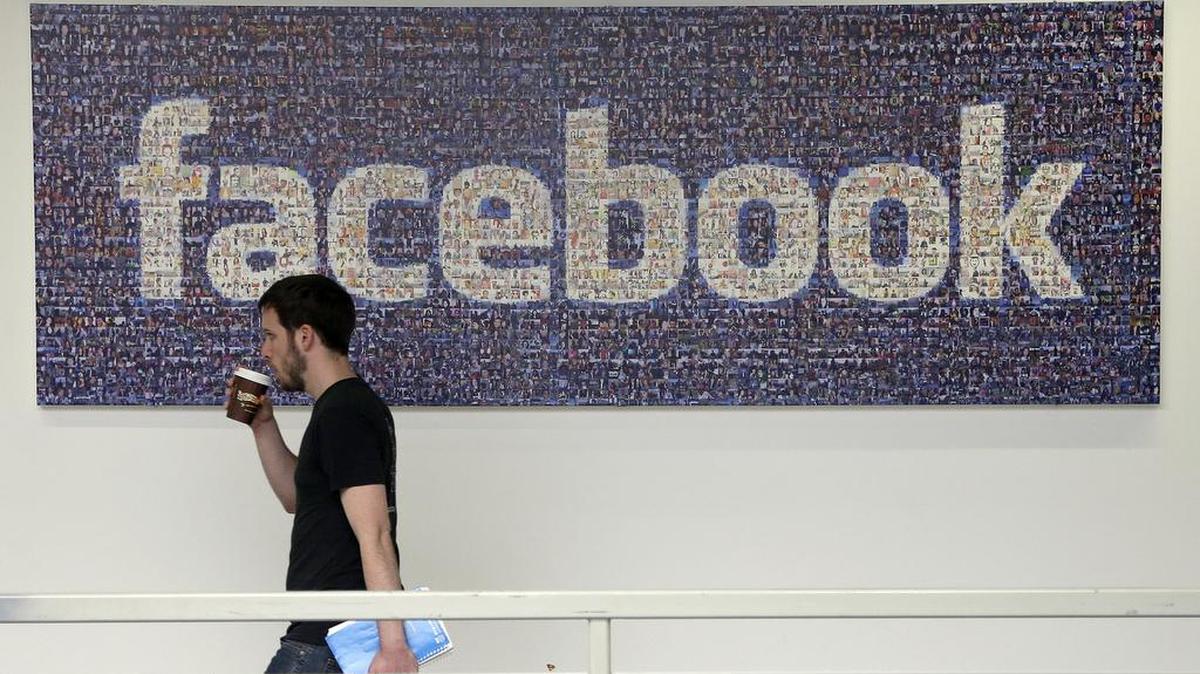 In this March 15, 2013, file photo, a Facebook employee walks past a sign at Facebook headquarters in Menlo Park, Calif.