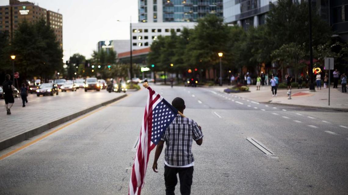 Skylar Barrett walks with an American flag in the middle of the street during a march through the Buckhead neighborhood against the recent police shootings of African-Americans on Monday in Atlanta.