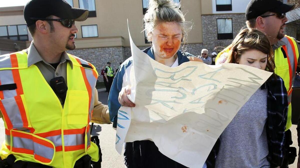 A girl protesting a Donald Trump rally is escorted by policeTuesday after being pepper sprayed by a man, while in a crowd of people in a confrontation between protesters and supporters of Trump outside the Holiday Inn Express, where Trump held a rally in Janesville, Wis.