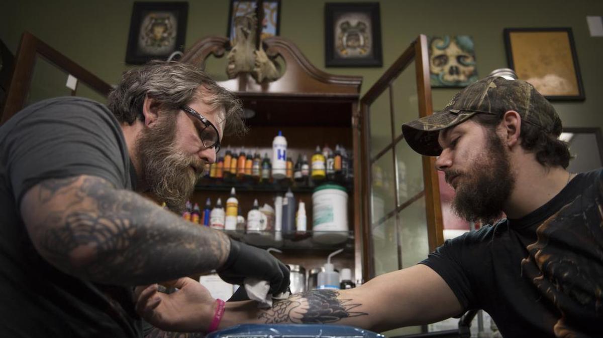 Tattoo parlor owner Dave Cutlip works on a tattoo on the arm of Randy Stiles.