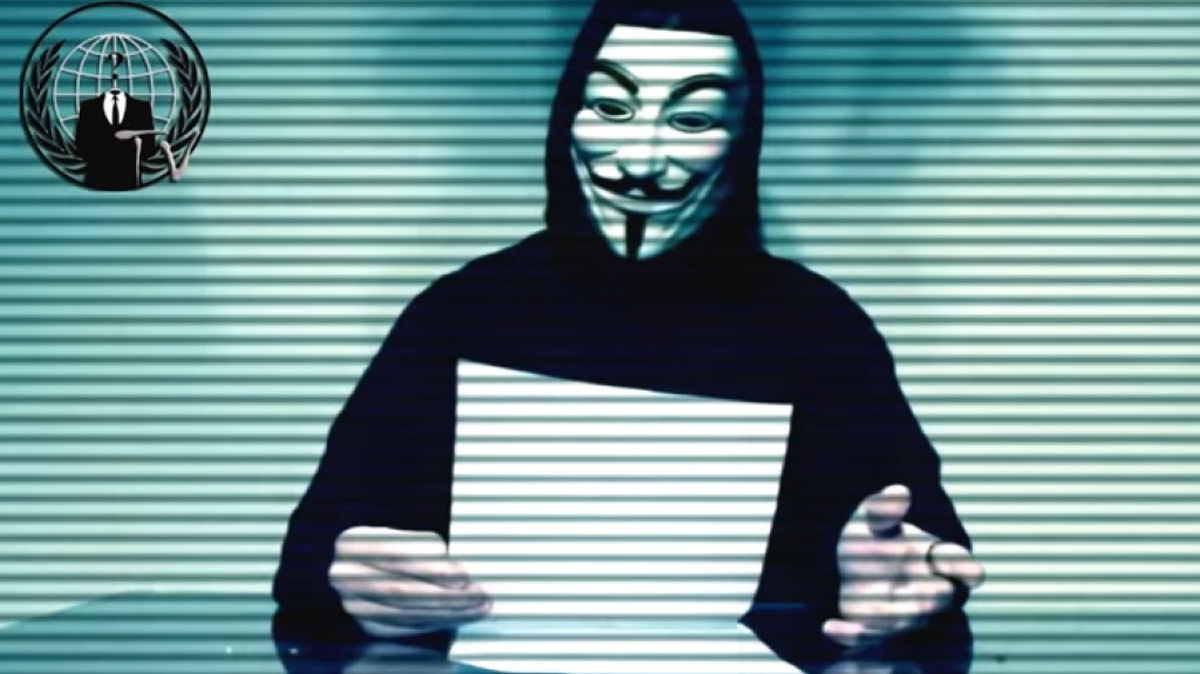 A person in a ghostly Guy Fawkes mask and dark robe reads the demands.