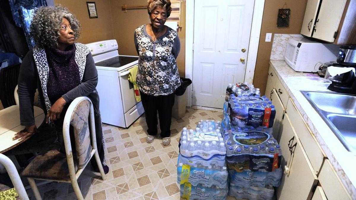 Anna Rushing, left, 73, and her sister, Nancy Watson, right, 72, both of Flint, talk about their itchy, red and dry skin symptoms they believe they received from the lead in Flint water as they talk Thursday near cases of bottled water in the kitchen.