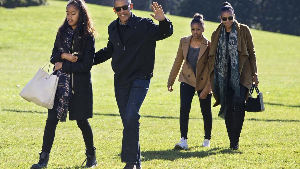 President Barack Obama waves as he walks across the South Lawn with daughter Malia, left, followed by Sasha Obama and first lady Michelle Obama on their return to the White House on Sunday, Jan. 3, 2016, after a family vacation in Hawaii.