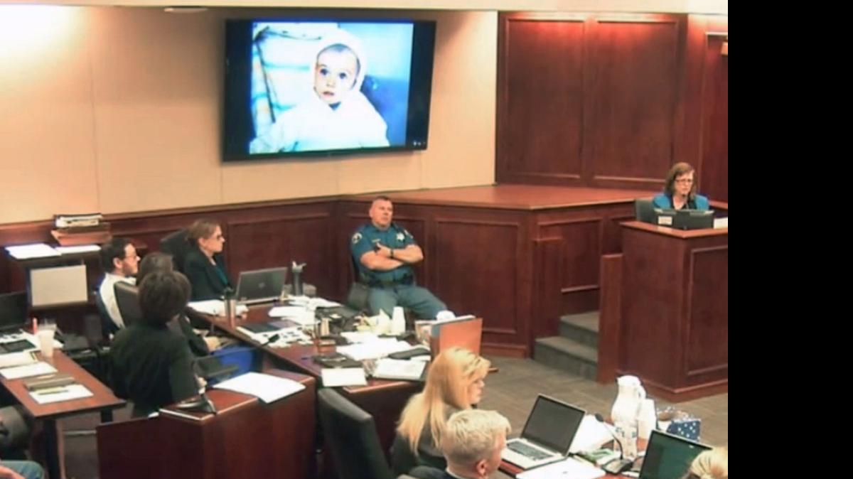 
In this July 29, 2015 file image made from Colorado Judicial Department video, a family photo is displayed on the screen showing James Holmes when he was a toddler, as James Holmes' mother Arlene, top right, gives testimony during the sentencing phase of the Colorado theater shooting trial in Centennial, Colo. James Holmes sits in court at far left. A fuller portrait of the Colorado movie theater shooter has emerged during Holmes' death penalty trial. Testimony given by Holmes' parents revealed a family laid bare by the tragic consequences of a son's incomprehensible descent from a well–behaved child with a quirky sense of humor into a killer capable of gunning down defenseless strangers. 

