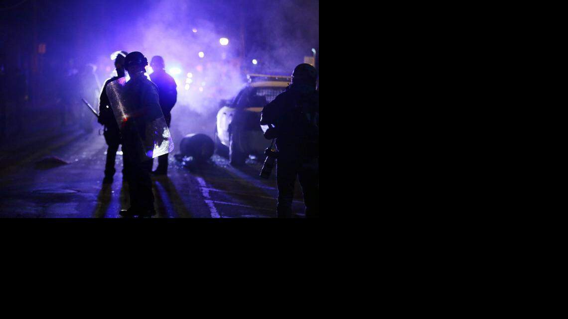 
Police officers watch protesters as smoke fills the streets in Ferguson, Mo., after the grand jury’s decision not to indict Officer Darren Wilson in the Aug. 9 shooting of Michael Brown on Nov. 25. 
