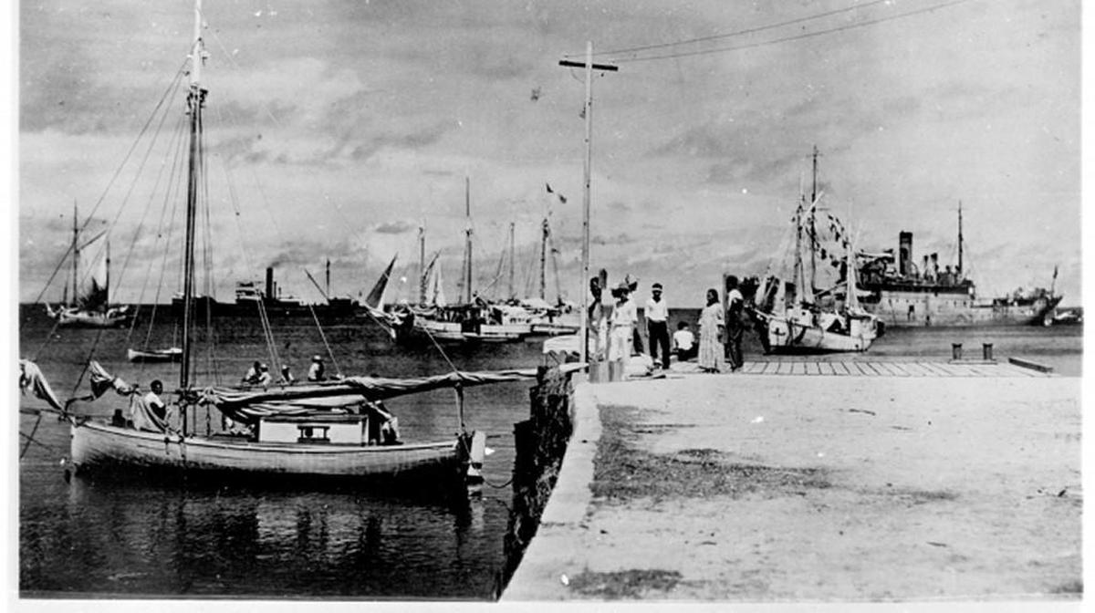 Amelia Earhart is believed to be the woman in the photo with short dark hair, wearing a white shirt, sitting on the dock with her head turned to the right.