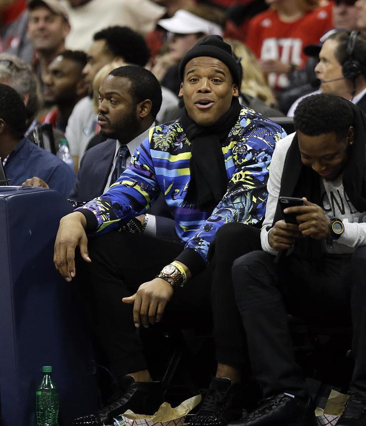 Carolina Panthers football player Cam Newton sits on the sidelines during the third quarter of an NBA basketball game between the Atlanta Hawks and the Oklahoma City Thunder, Friday, Jan. 23, 2015, in Atlanta.