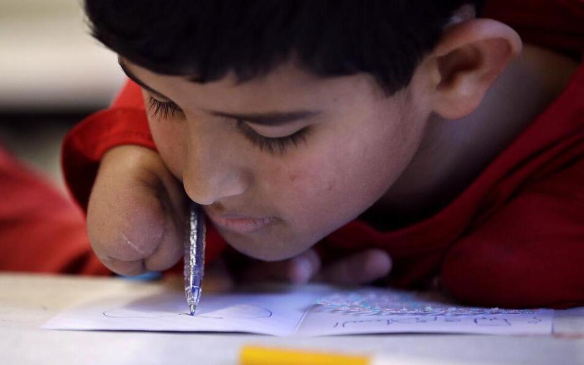 Syrian refugee Ahmad Alkhalaf draws a heart while making a card for refugee children displaced in Syria during a day camp for local Muslim children in Sharon, Mass. Ahmad lost his arms in a refugee camp bomb blast but is thriving in his new life in Massachusetts.