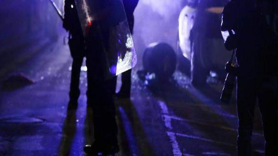 
In this Nov. 25, 2014 file photo, police officers watch protesters as smoke fills the streets in Ferguson, Mo., after a grand jury’s decision in the fatal shooting of Michael Brown. A Justice Department investigation has found patterns of racial bias in the Ferguson police department and at the municipal jail and court. The full report, to be publicly released on March 4, says the investigation found Ferguson officers disproportionately used excessive force against blacks and too often charged them with petty offenses. 
