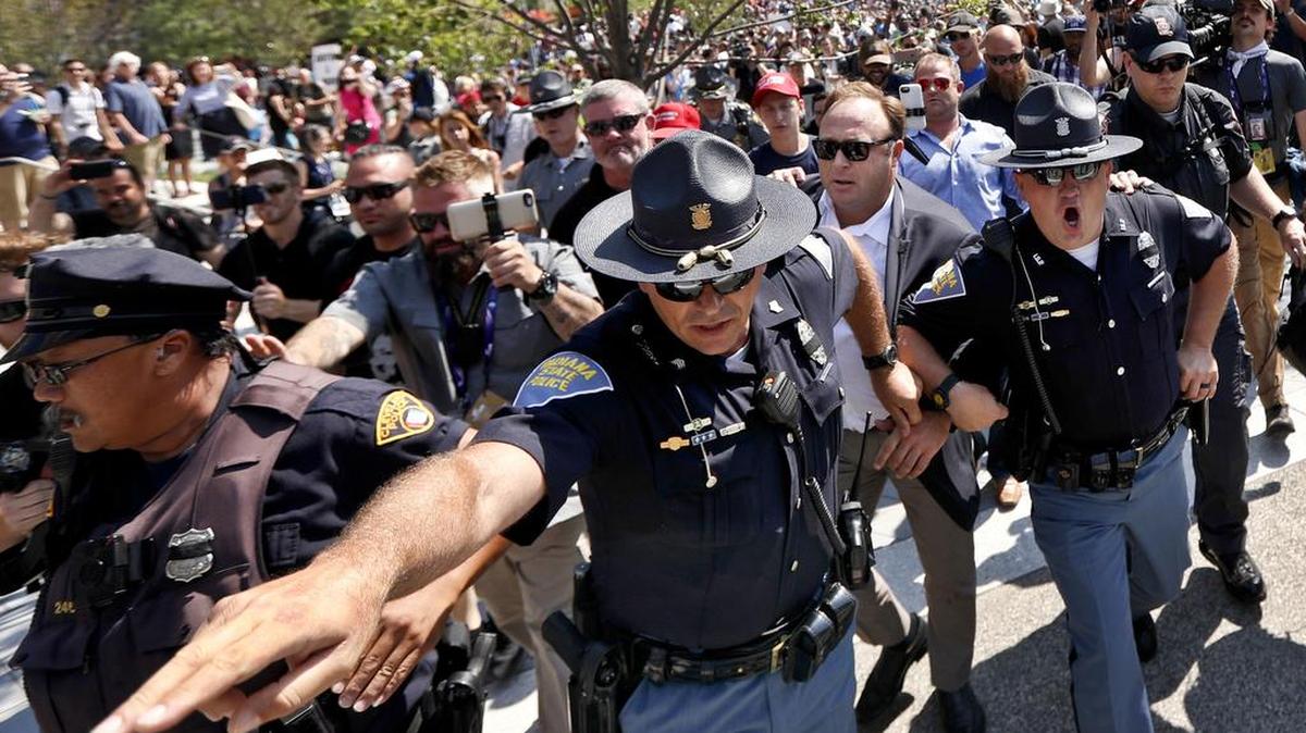 Alex Jones, second from right, is escorted by police from a crowd of protesters last July after he said he was attacked in Public Square in Cleveland during the second day of the Republican National Convention.