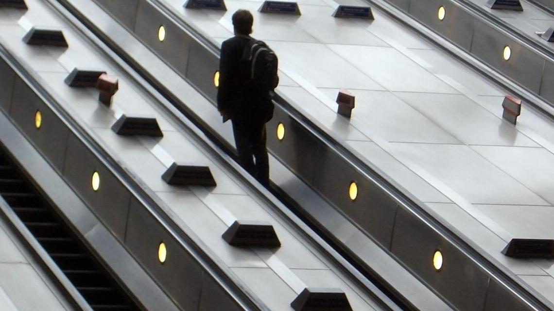 A man stands on an escalator at Canary Wharf.