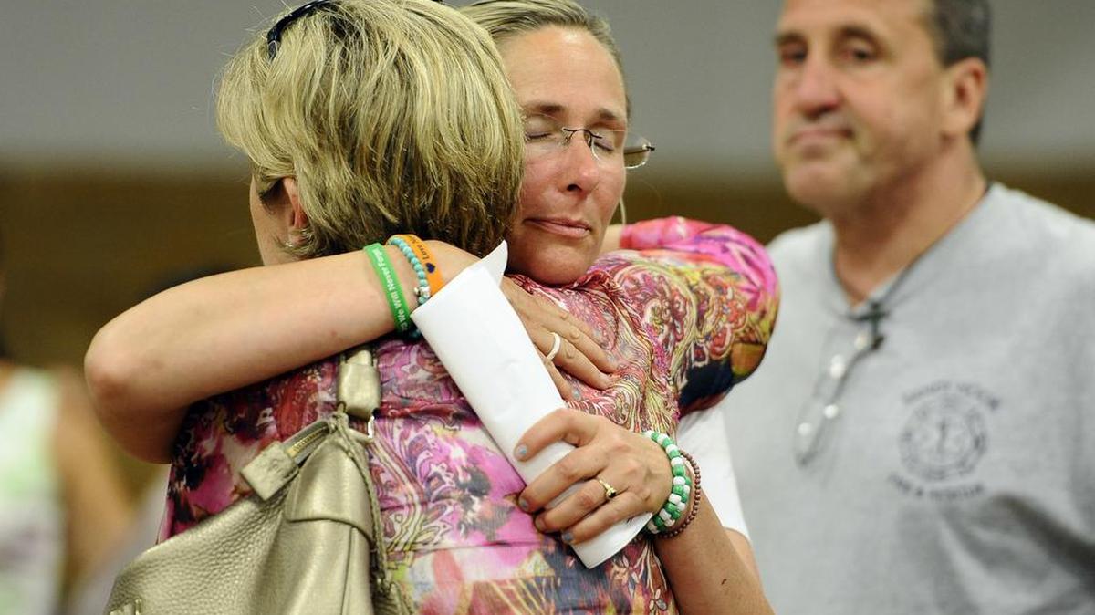 In this 2013 photo, Scarlett Lewis, mother of Sandy Hook Elementary School shooting victim Jesse Lewis, center, hugs Lynn McDonnell, mother, of victim Grace McDonnell, left, as Neil Heslin, father of victim Jesse Lewis, right, looks on after a public forum on the distribution of Newtown donations at Edmond Town Hall in Newtown, Conn.