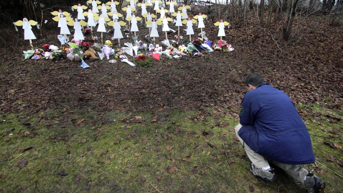 Robert Soltis, of Newtown, Conn., pauses after making the sign of the cross at a memorial to Sandy Hook Elementary School shooting victims in Newtown in 2012. A Florida Atlantic University professor faces possible termination over his arguments that the attack was staged and alleged harassment of the parents of one of the 26 children killed at the school.