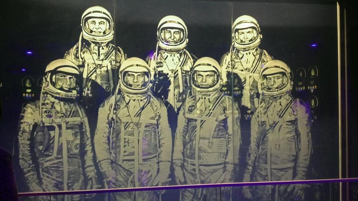 Painted on glass, this artwork represents NASA’s Mercury 7 astronauts: Scott Carpenter, Gordon Cooper, John Glenn, Gus Grissom, Wally Schirra, Alan Shepard, and Deke Slayton. A large fiberglass sculpture of the image is on the building’s facade.
