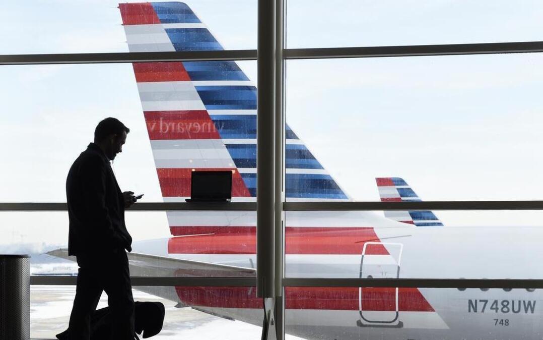 In this Jan. 25, 2016, file photo, a passenger talks on the phone as American Airlines jets sit parked at their gates at Washington's Ronald Reagan National Airport. After 15 years of cutbacks, U.S. airlines are starting to add back some small perks for everyday coach passengers.