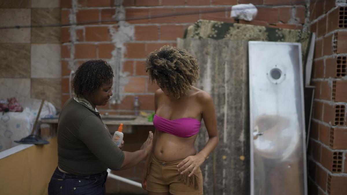 Renata Cristina da Costa, left, spreads repellent on her daughter Tamires da Costa, 16, who's four months pregnant, at their home in the Parque Sao Bento a shantytown of Rio de Janeiro, Brazil, Friday, Jan. 29, 2016. Thanks to Aedes aegypti modquito, the Zika virus quickly spread across Brazil and to more than 30 countries and territories in the region. (AP Photo/Leo Correa)
