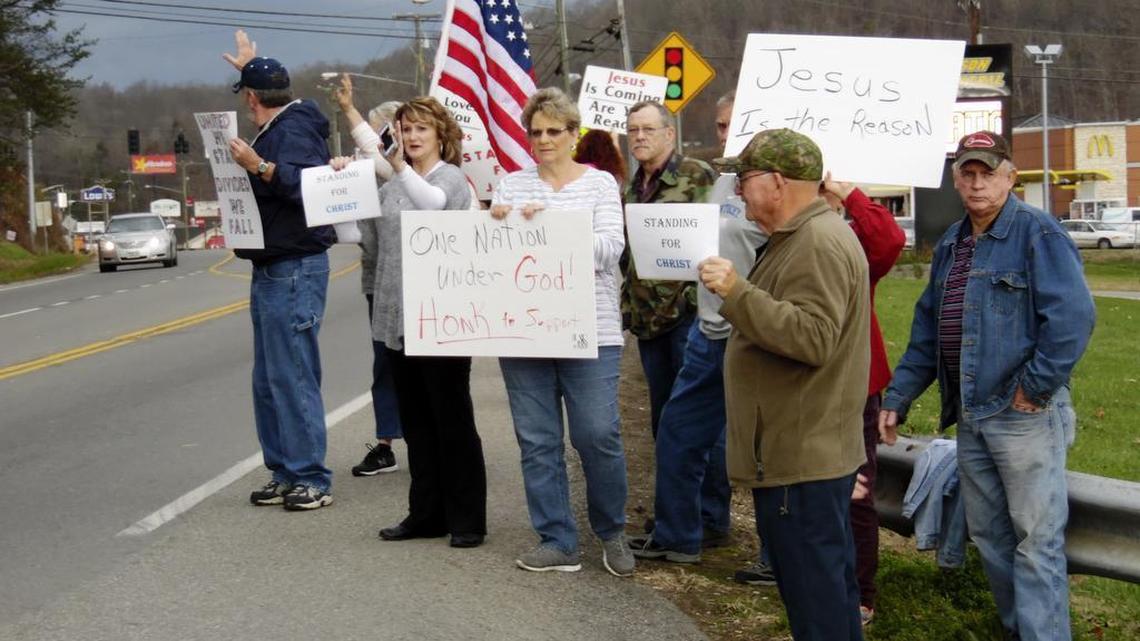 Protesters carrying signs and waving banners stood outside the Johnson County Board of Education office Monday to oppose removal of religious references from school plays and other programs.
