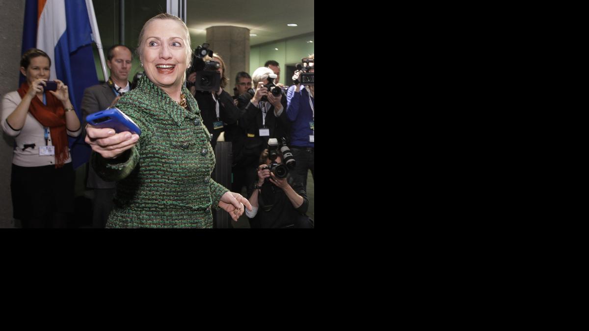 
Then-U.S. Secretary of State Hillary Rodham Clinton hands off her mobile phone after arriving to meet with Dutch Foreign Minister Uri Rosenthal at the Ministry of Foreign Affairs in The Hague, Netherlands on Dec. 8, 2011. 
