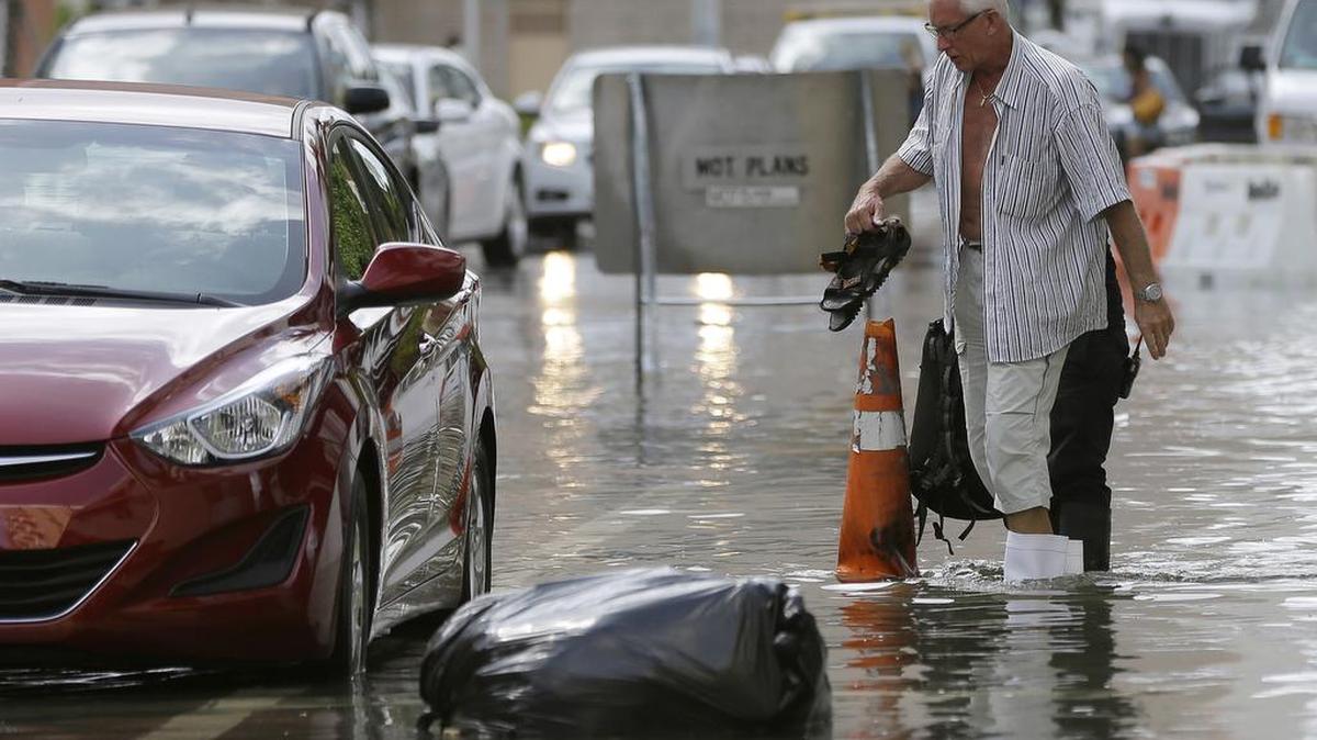 
A hotel guest carries his shoes as he is escorted to his car along a flooded Collins Ave., Wednesday, Sept. 30, 2015, in Miami Beach, Fla. The street flooding was in part caused by high tides due to the lunar cycle, according to the National Weather Service. 
