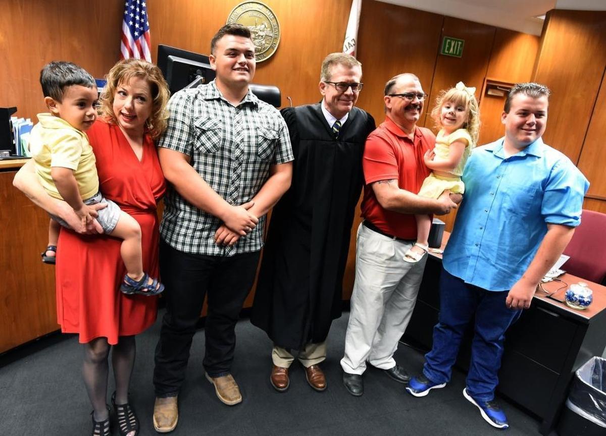 Carson Petersen poses for a photo with Fresno County Superior Court Commissioner Gary Green and his adoptive family, from left: brother Joshua, mother Renee Petersen, father Tex Peterson, sister Kaylynn, and brother Hunter, after the hearing.