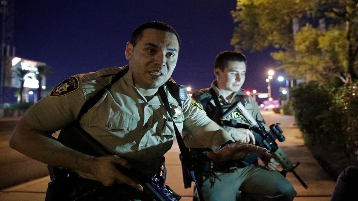 On the Las Vegas Strip, police officers advise people to take cover near the scene of a mass shooting outside the Mandalay Bay resort and casino on Sunday, Oct. 1.