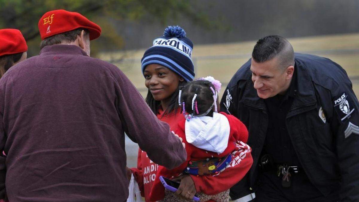 Shakira Henderson receives money from a Secret Santa on Remount Road as CMPD Sergeant Charles Rappleyea entertains her one year old daughter Zyerra, Tuesday, December 01, 2015.