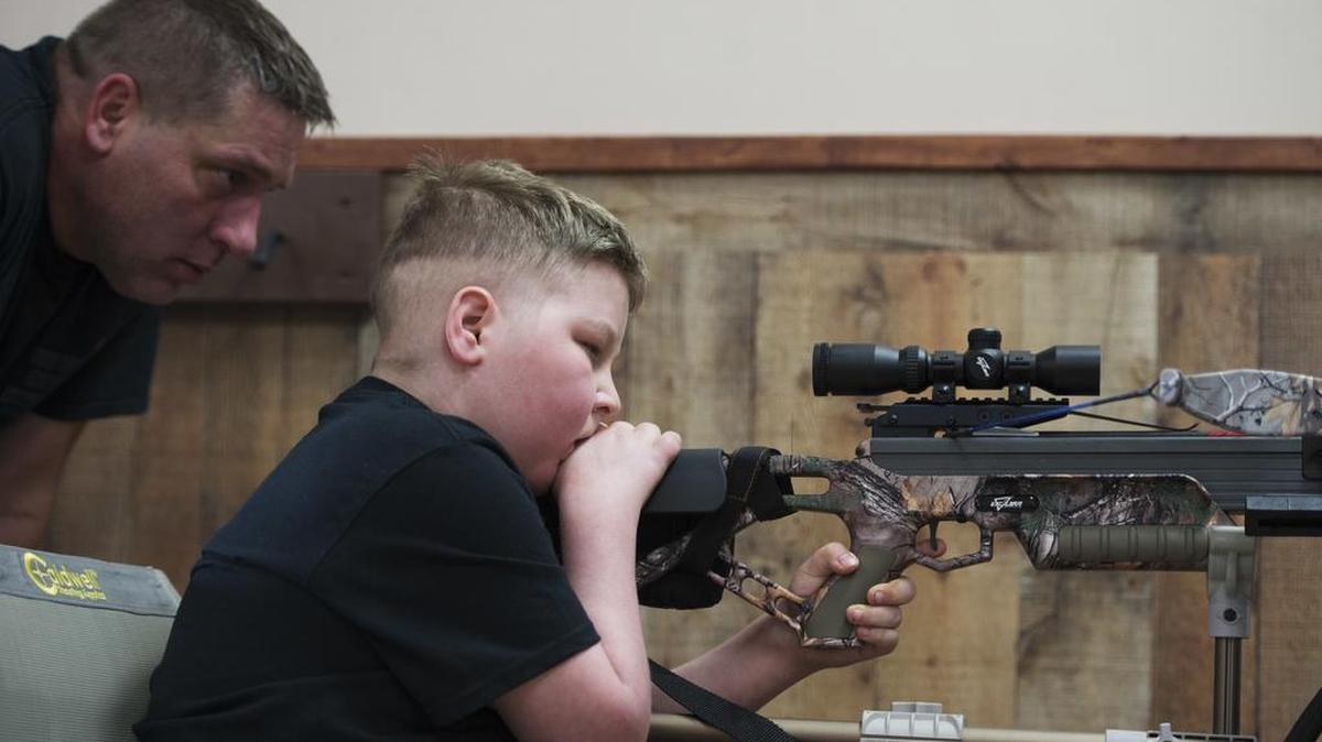 Bill Kohler watches over his son Ayden’s shoulder as he shoots a target at X-Treme Archery in Springettsbury Township, Pa. Though cancer has limited his mobility, a special chair with an extended arm helps stabilize the bow so Ayden can still shoot.