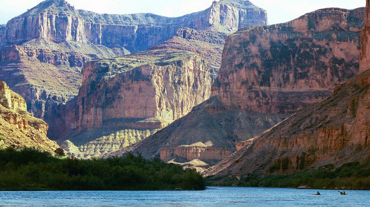 Kayakers glide through the Colorado River near Grand Canyon National Park as the canyon's walls rise up hundreds of feet around them.