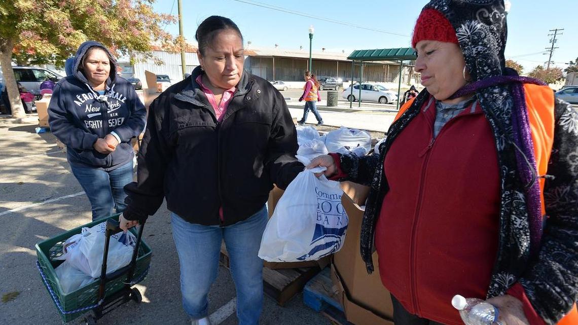 Food bank volunteer Martha Aguilera, right, of Huron, hands bags of fresh produce to Maria Lopez, 43, center, and her cousin Reyna Camacho, 45, left, both of Huron, as part of a Community Food Bank drought relief package on Nov. 16 in Huron. A seasonal farmworker, Lopez just finished working the lettuce harvest. She doesn’t expect to find more farm work until January, at the earliest. To get the food packages, workers must either have had their hours reduced or have lost their job because of the drought.