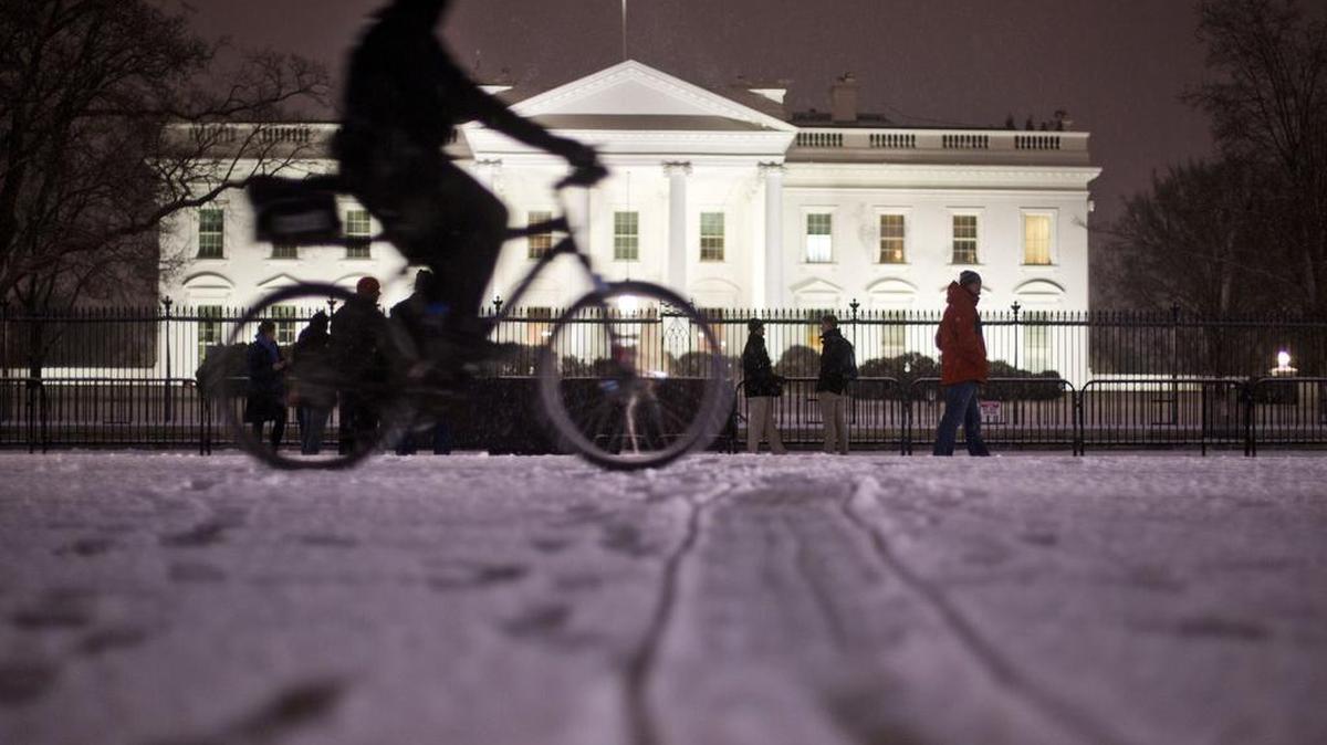 A bicyclist rides past the White House during evening snowfall in Washington on Wednesday. As Washington prepares for this weekend's snowstorm, now forecast to reach blizzard conditions, a small clipper system pushed through the region Wednesday night causing massive delays and issues on the roads.
