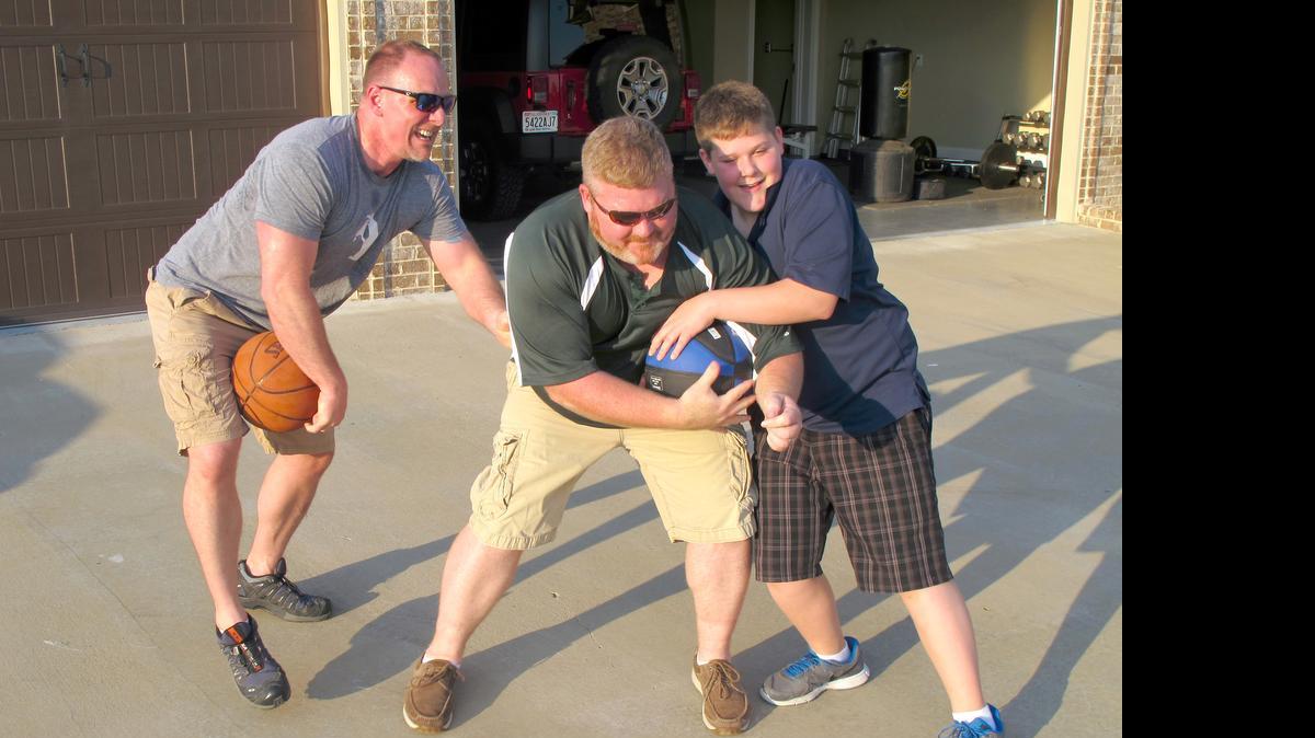 
Brett Jones, left, the first openly gay Navy SEAL, plays basketball with his husband, Jason White, and their son, Ethan, 13, outside their Alabama home. 
