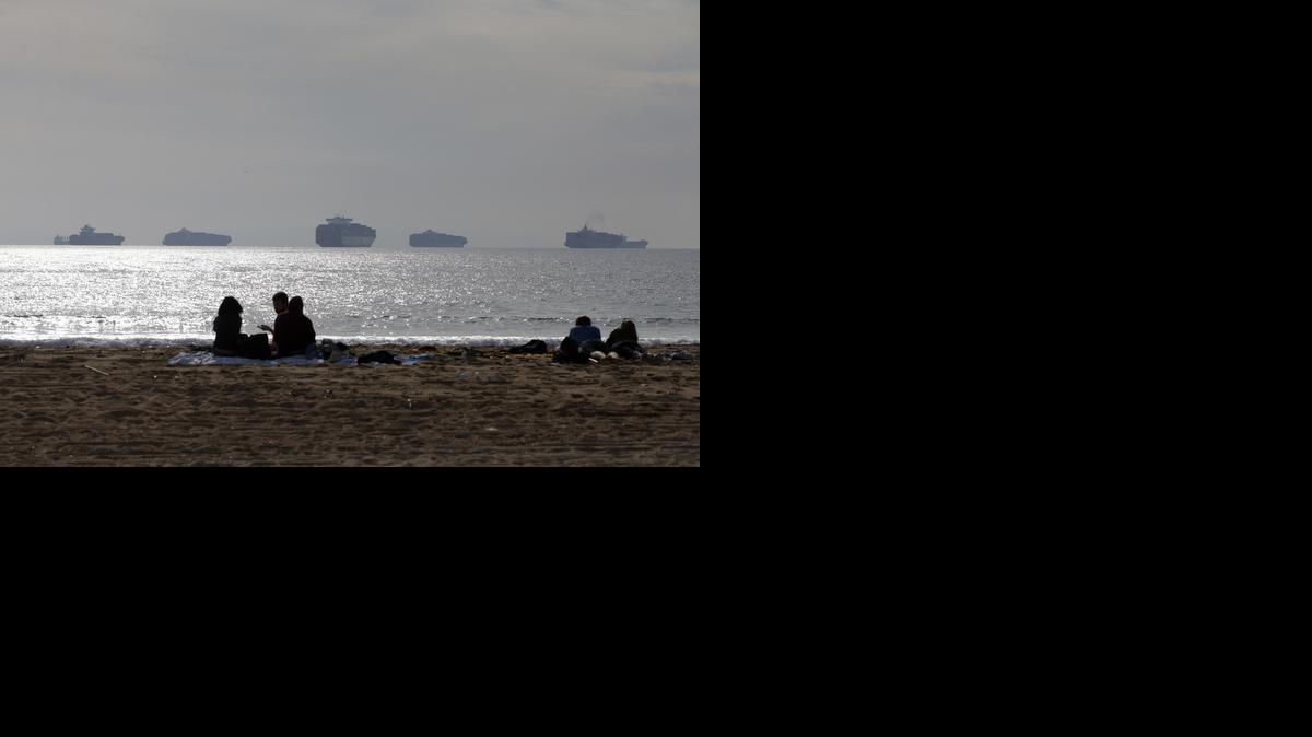 
People relax on the beach, Friday, Feb. 20, 2015, in Sunset Beach, Calif., as loaded cargo ships are anchored outside the Ports of Long Beach and Los Angeles. Billions of dollars of cargo are sitting on dozens of massive ships anchored outside West Coast ports. They cannot dock because of historically bad cargo bottlenecks at 29 ports that handle about $1 trillion of trade annually, much of it with Asia.

