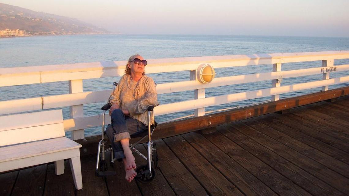In this 2012 photo provided by David Chick, actress Holly Woodlawn sits on Fisherman's Pier in Malibu, Calif. Woodlawn, who starred in the 1970 Paul Morrissey film "Trash" and was immortalized in the first few lines of Lou Reed's "Walk on the Wild Side," died Sunday, Dec. 6, 2015, in Los Angeles after a battle with cancer. She was 69.