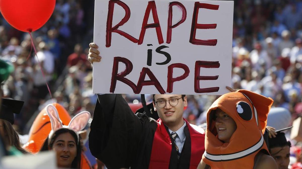 Paul Harrison, center, carries a sign of protest during Stanford University graduation exercises at Stanford Stadium, on Sunday. A juror in the trial of Brock Turner, who was sentenced to six months in jail for rape, said he was appalled by the lenient sentence.