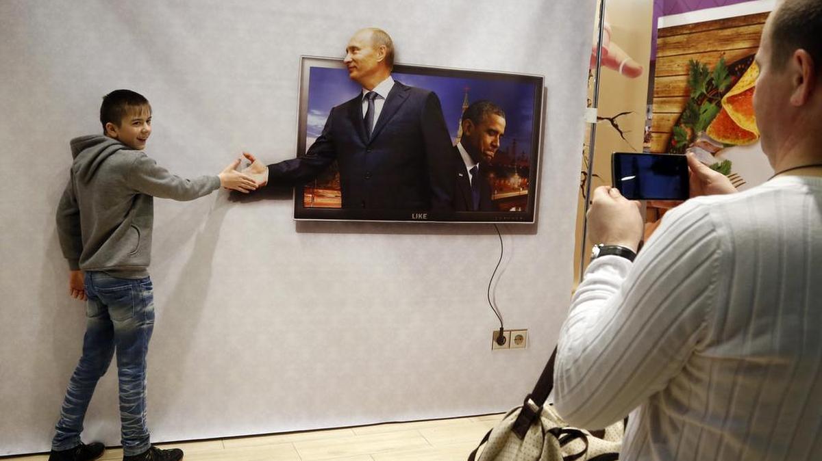 A boy poses for a photo with a poster depicting Russian President Vladimir Putin, left in photo, and U.S. President Barack Obama in a shopping mall in St.Petersburg, Russia, on Sunday, Jan. 3, 2016.