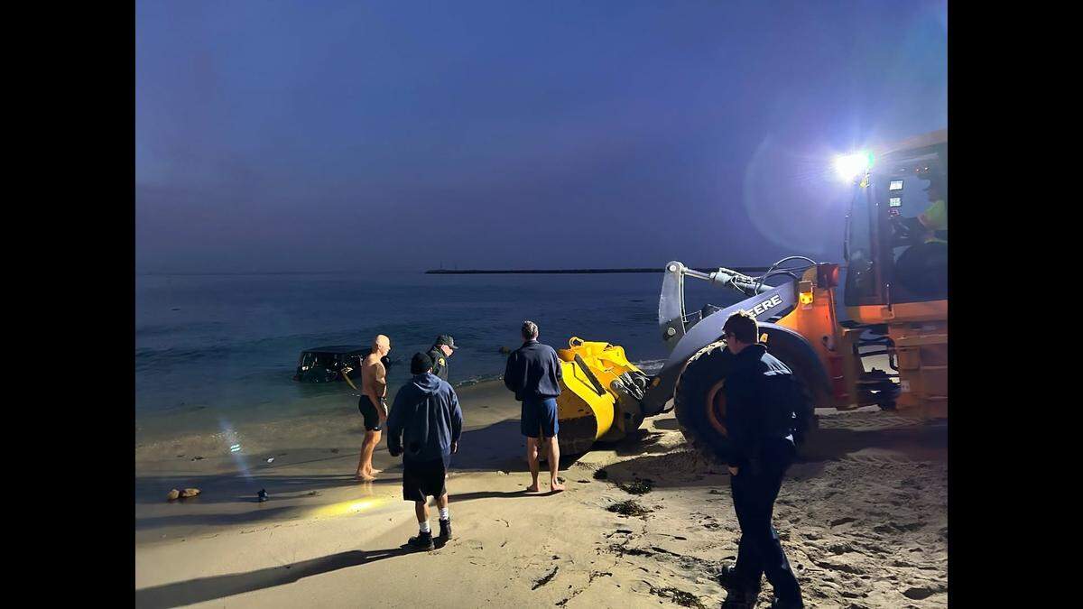 Heavy equipment is used to pull a Jeep out of the water at Corona Del Mar Beach in California.